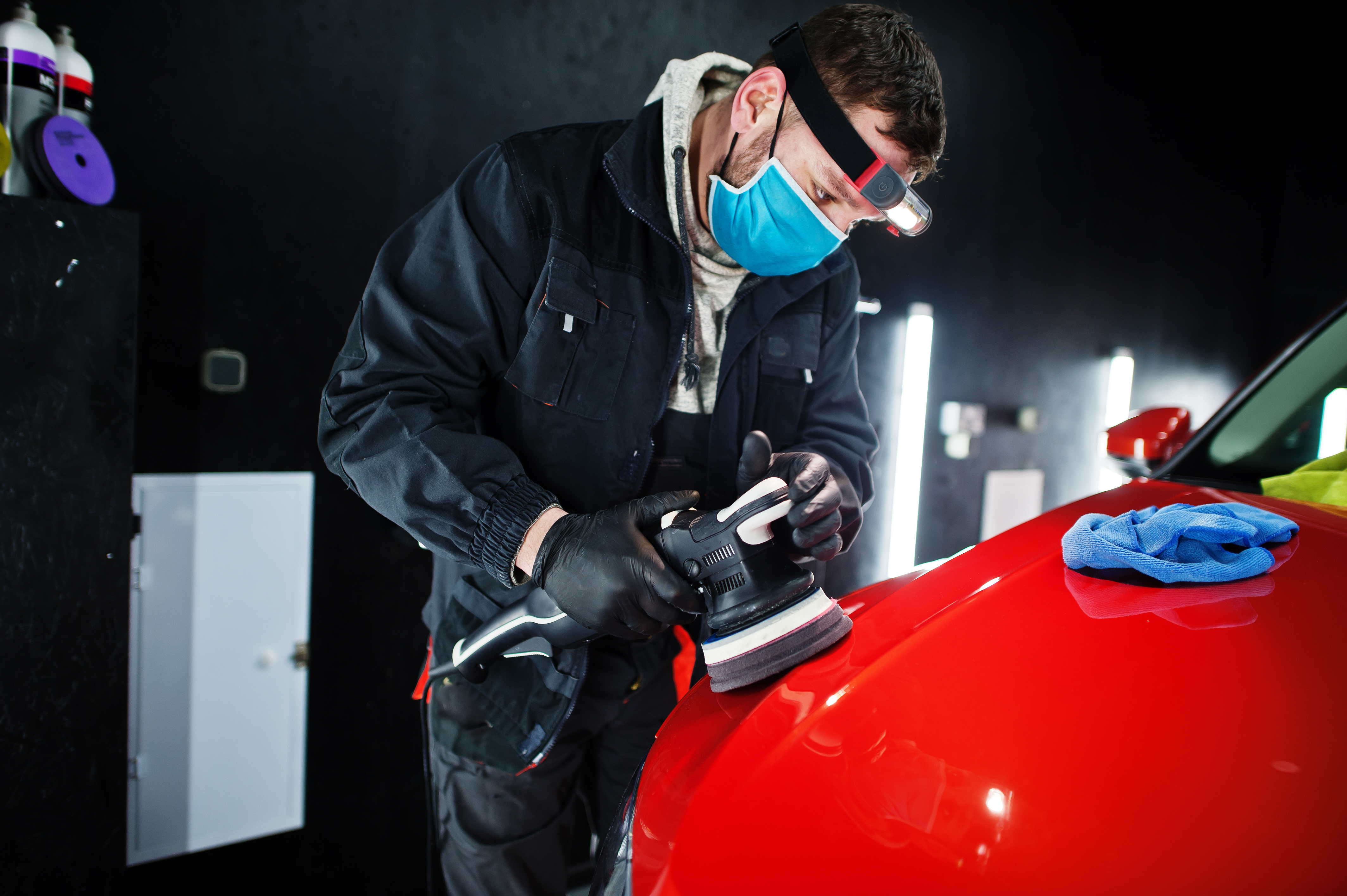 car-detailing-concept-man-face-mask-with-orbital-polisher-repair-shop-polishing-orange-suv-car